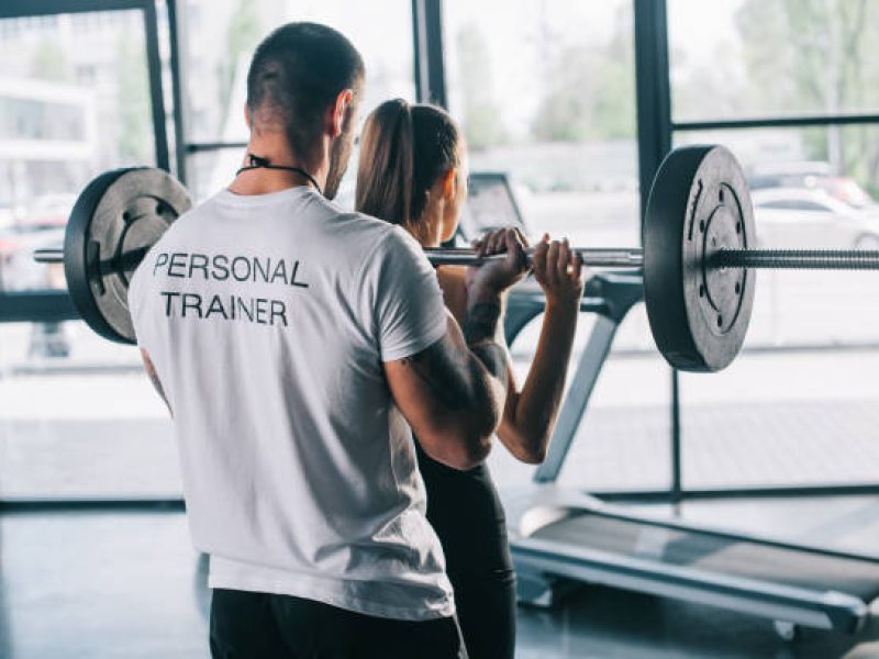 male personal trainer helping sportswoman to do exercises with barbell at gym